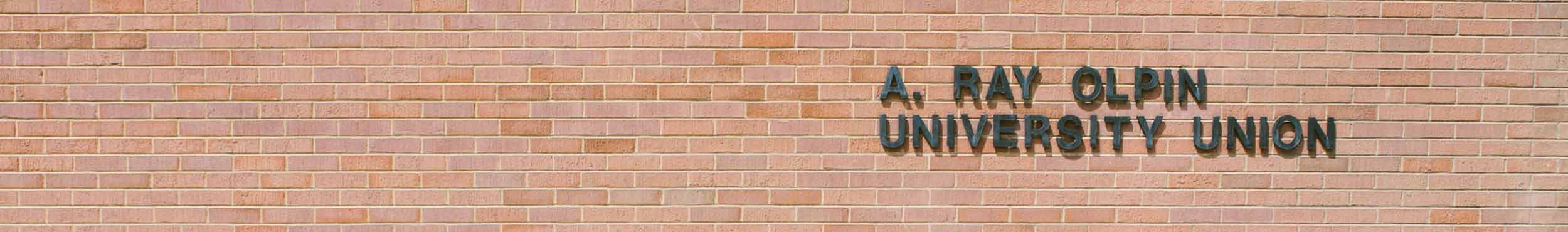 A photo of a brick wall with metal words "A. Ray Olpin University Union" mounted into the brick.